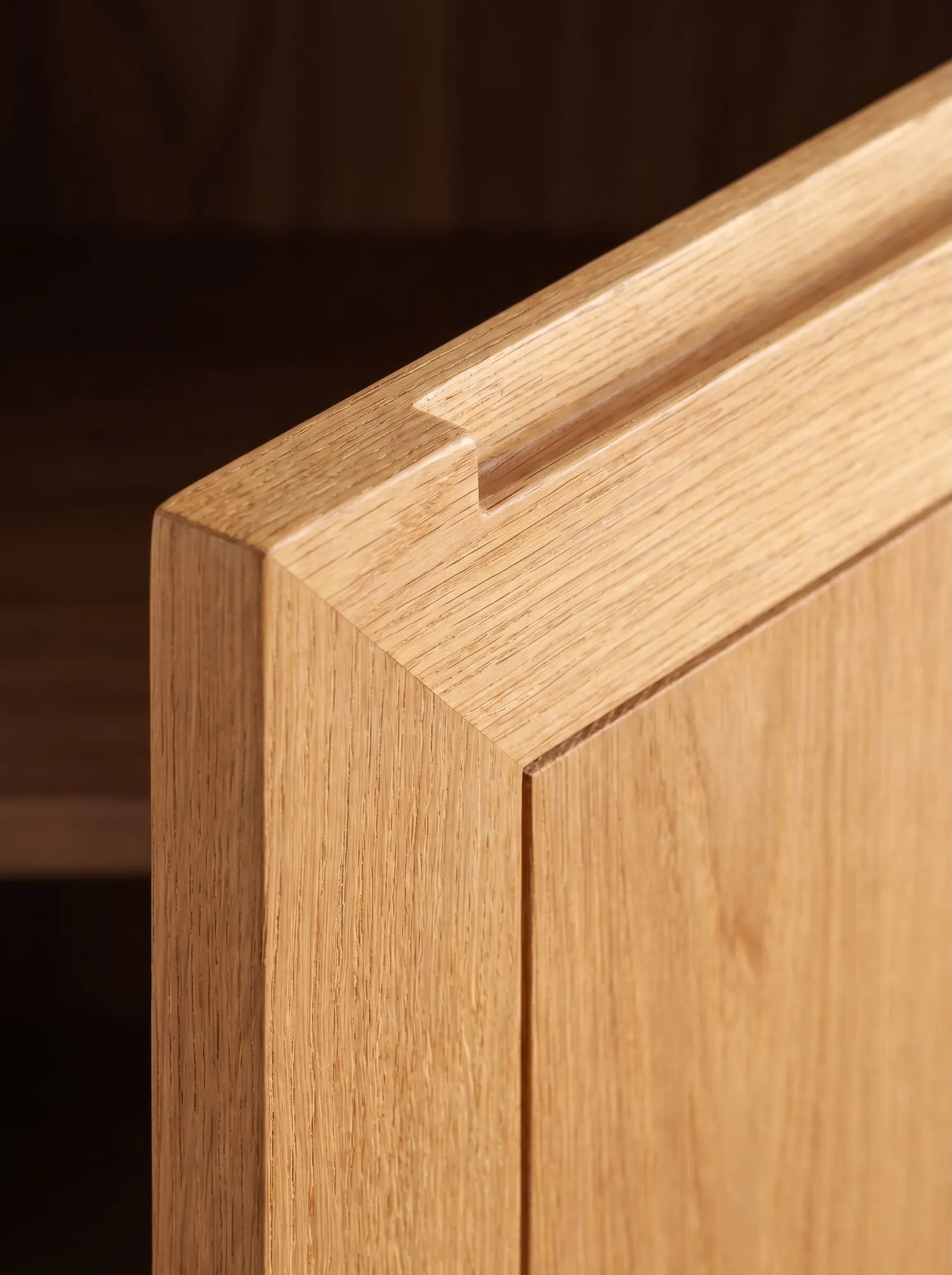 Close-up of oak cabinet door detail with integrated handle and precise joinery